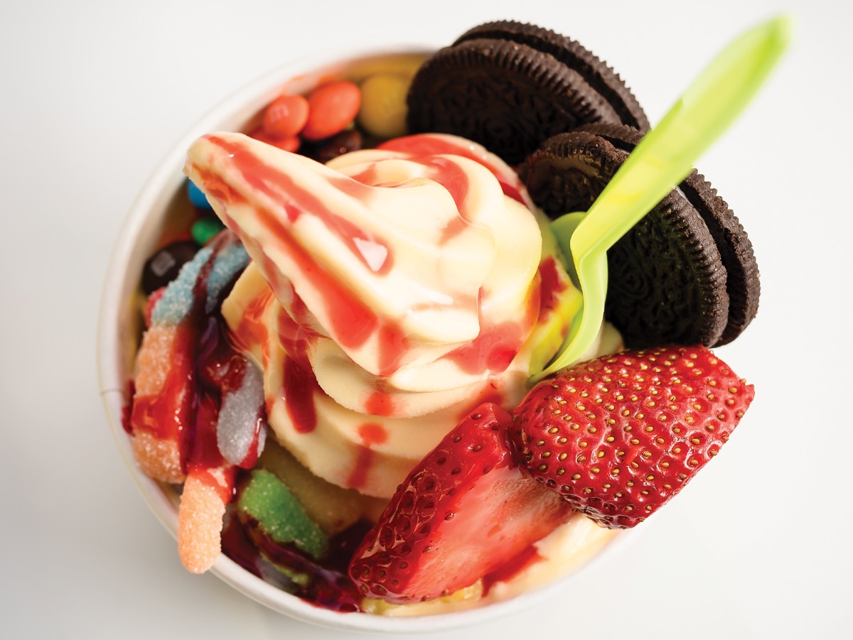 A cup of swirled frozen yogurt topped with strawberries, cookies and gummy candy