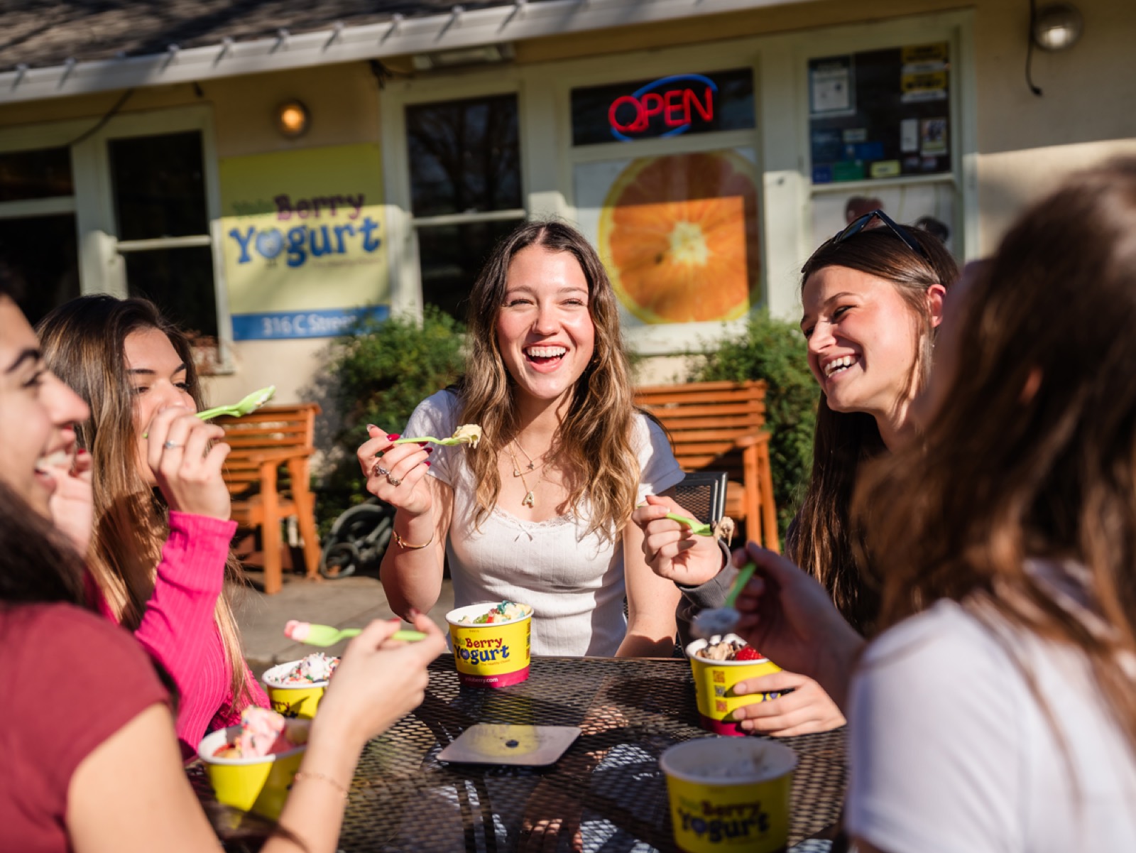 Friends laughing over frozen yogurt cups on the patio outside YoloBerry Yogurt in Davis
